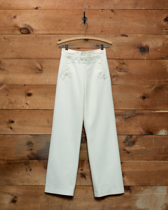 Cream-colored Riding Twill Sailor Trousers with a button-front closure hanging on a wooden hanger.