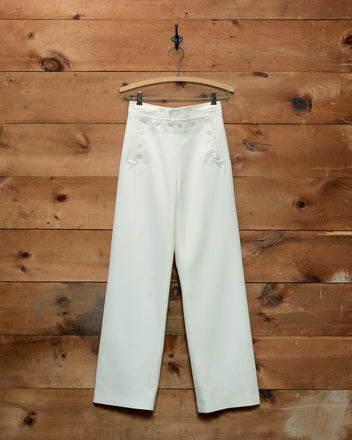 Cream-colored Riding Twill Sailor Trousers with a button-front closure hanging on a wooden hanger.